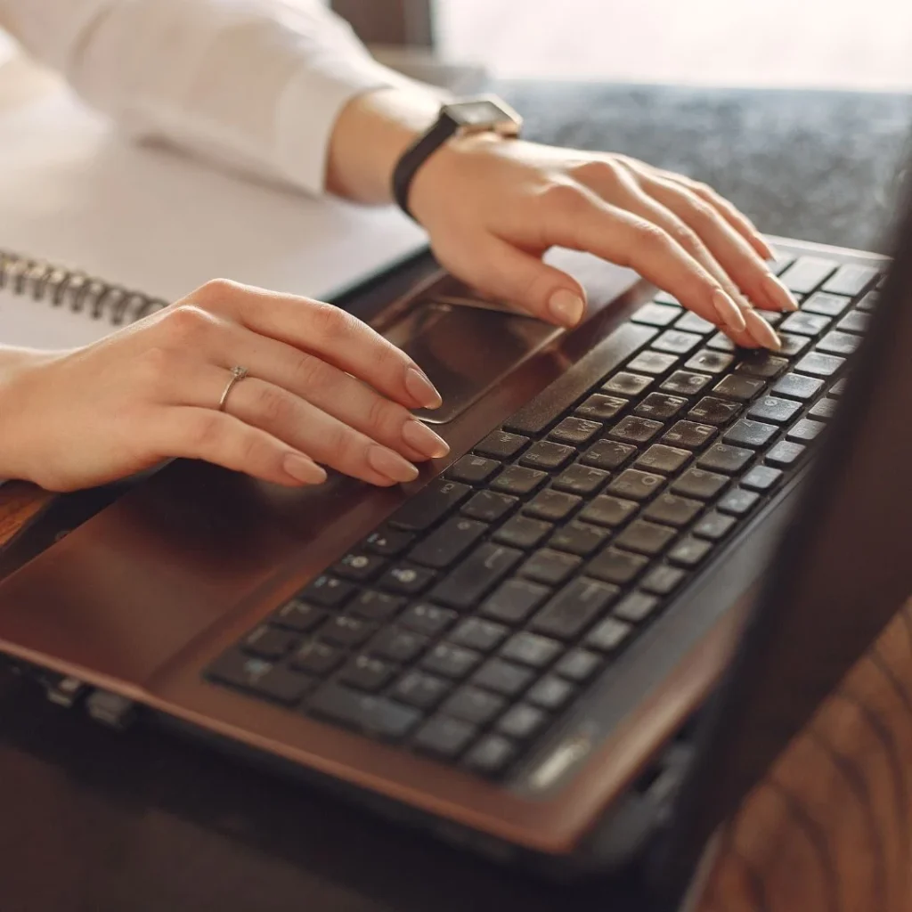 Close-up of a woman's hands typing on a laptop keyboard.